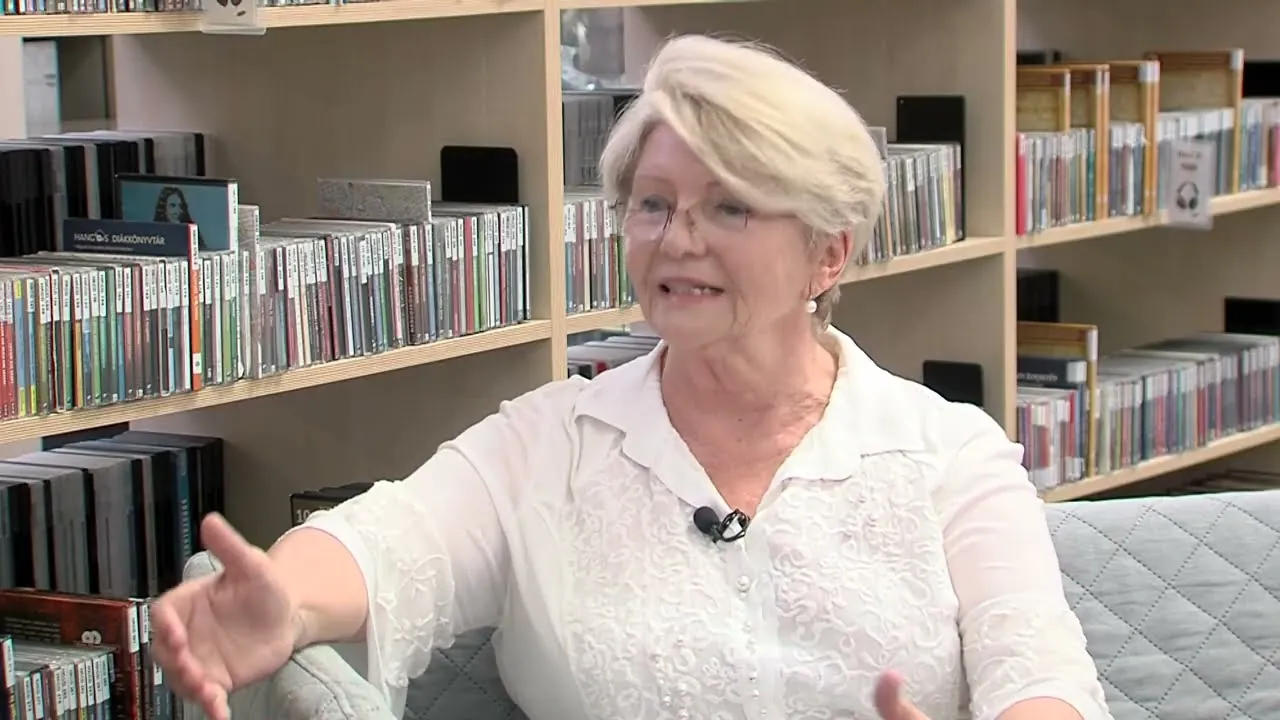Fazekasné Visnyei Irma interjút ad a Tolnatáj Televíziónak egy könyvtárban